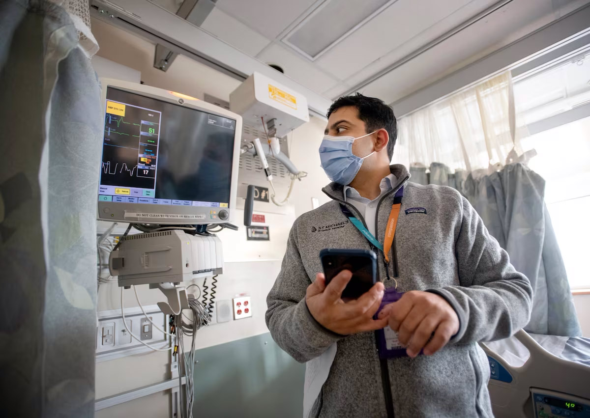 Masked clinician looks at a monitor with a phone prompt in his hand